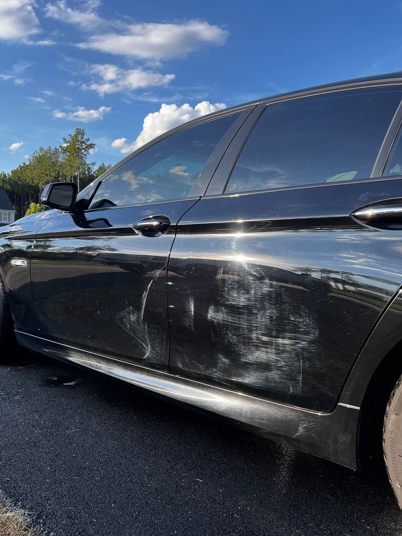 Black BMW side panel with heavy scratches and swirl marks before paint correction